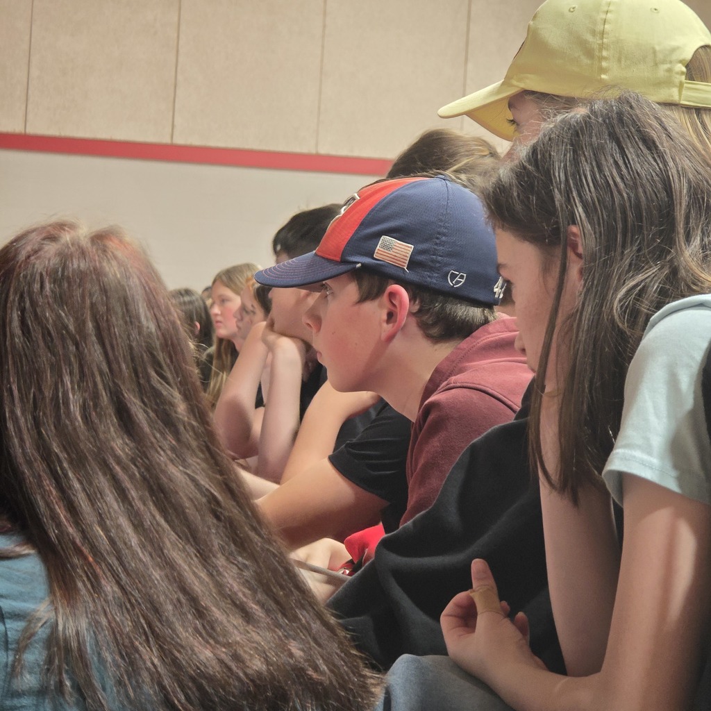 People sitting in rows, one wearing a blue hat with a red and white stripe. A red line is along the top of the wall.