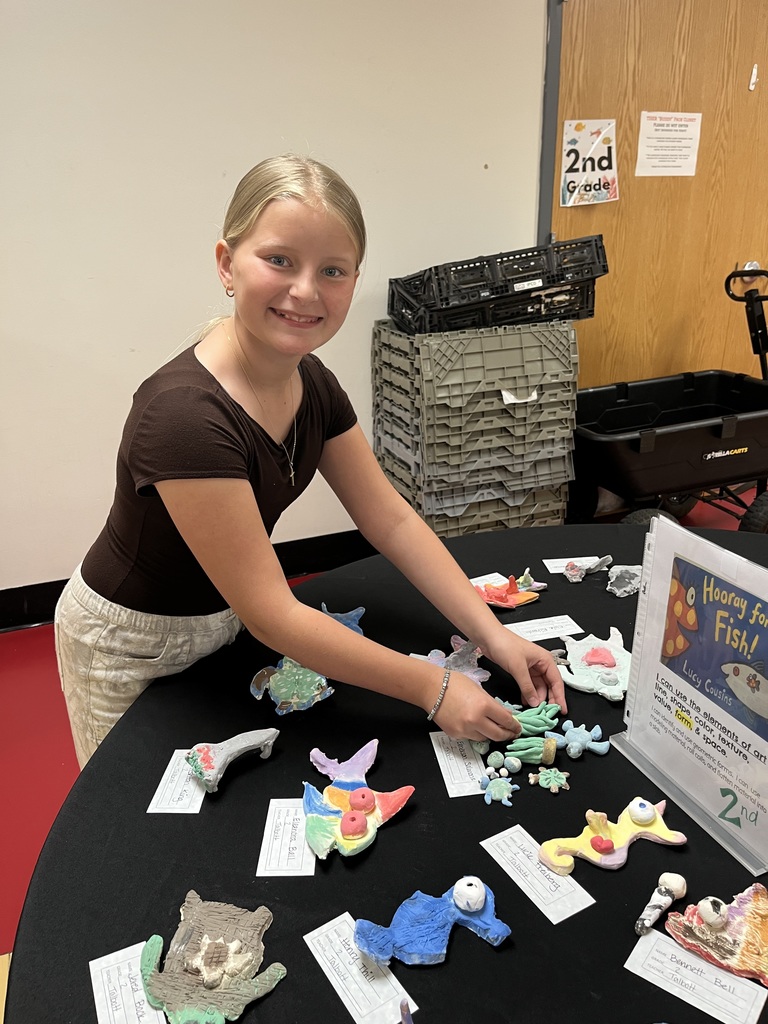 A girl in a brown top and beige pants standing at a table with a display of toy animals.