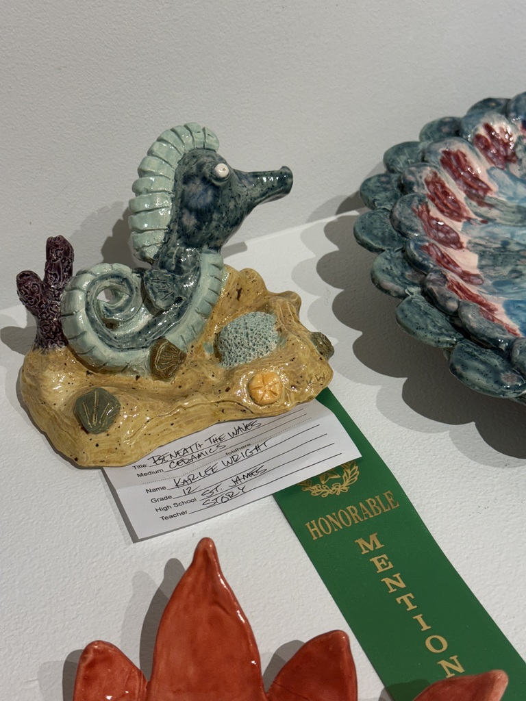 Display of ceramic items on a white table. A small seahorse figurine is on a base, next to a large shell-like item.