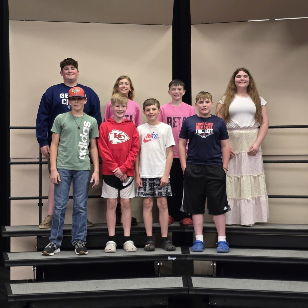 A group of people stand on a stage, some wearing casual clothing and sneakers, others in dresses.