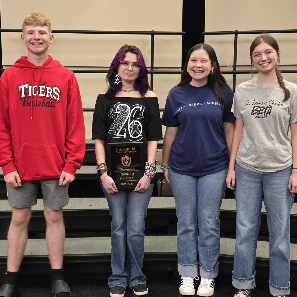 Four people stand on a stage in front of a row of steps, wearing different colored shirts.