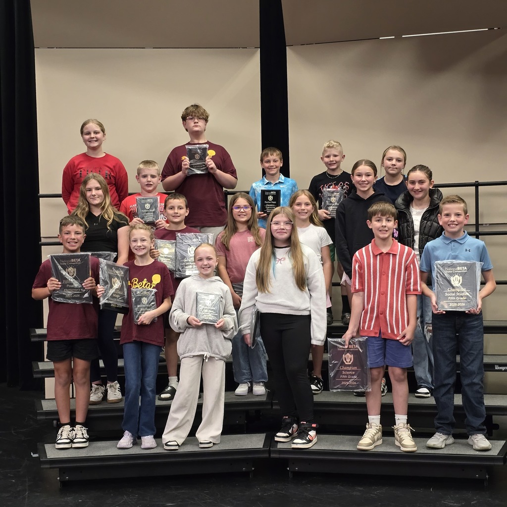 A group of young students on stage, each holding an award, smiling, with a black curtain in the background.