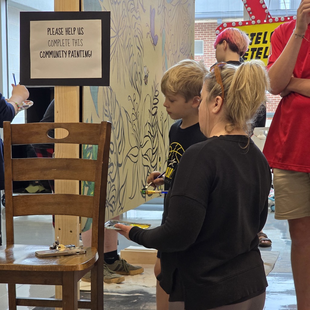 People paint on a wall with a sign asking for help. A wooden chair has a plate on it.