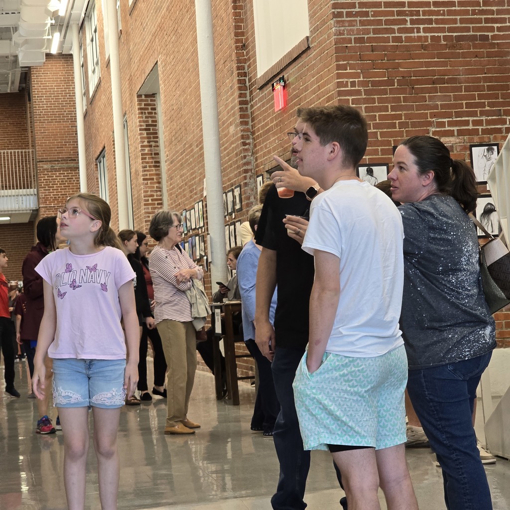 People stand inside a building with brick walls and shiny floors. A girl and man face each other.