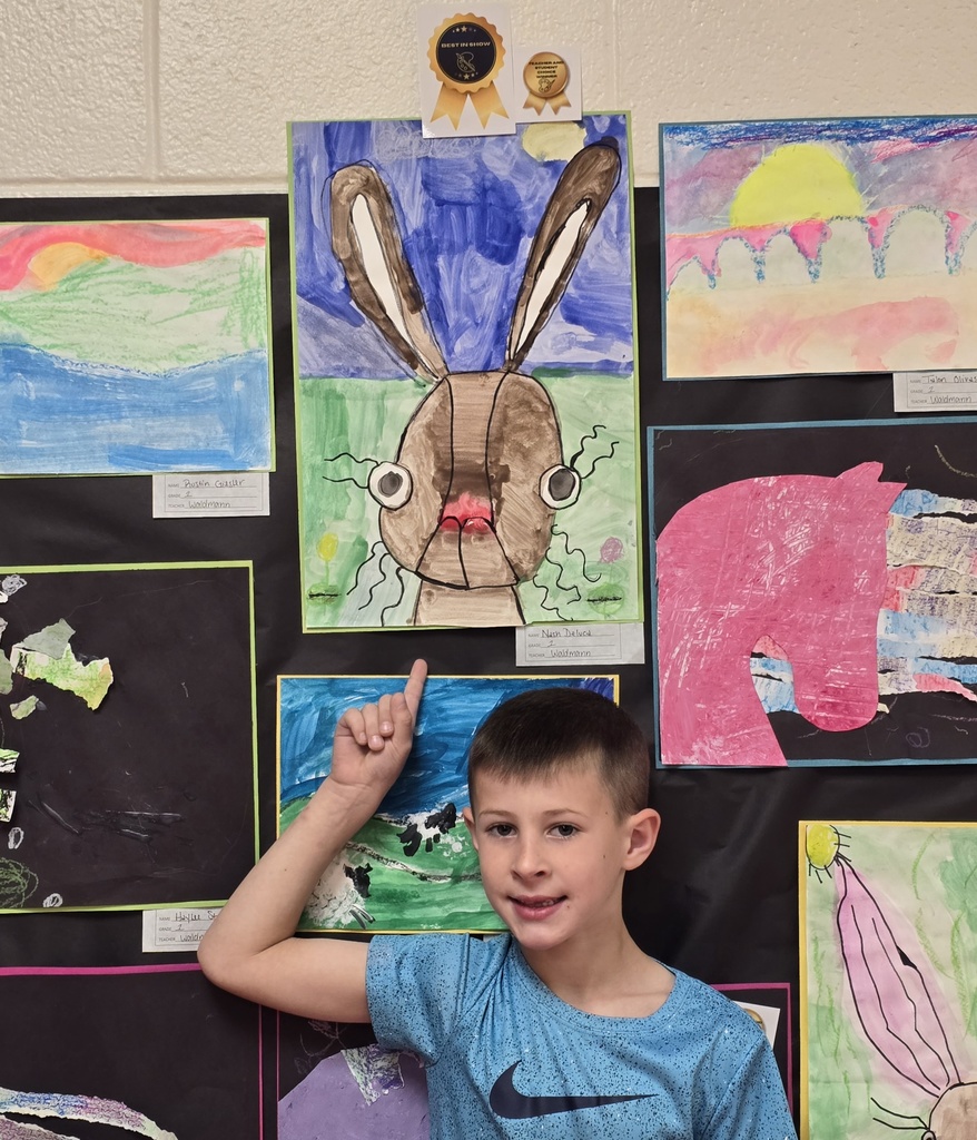 A young boy points at a rabbit drawing on a classroom bulletin board with various colorful artwork.