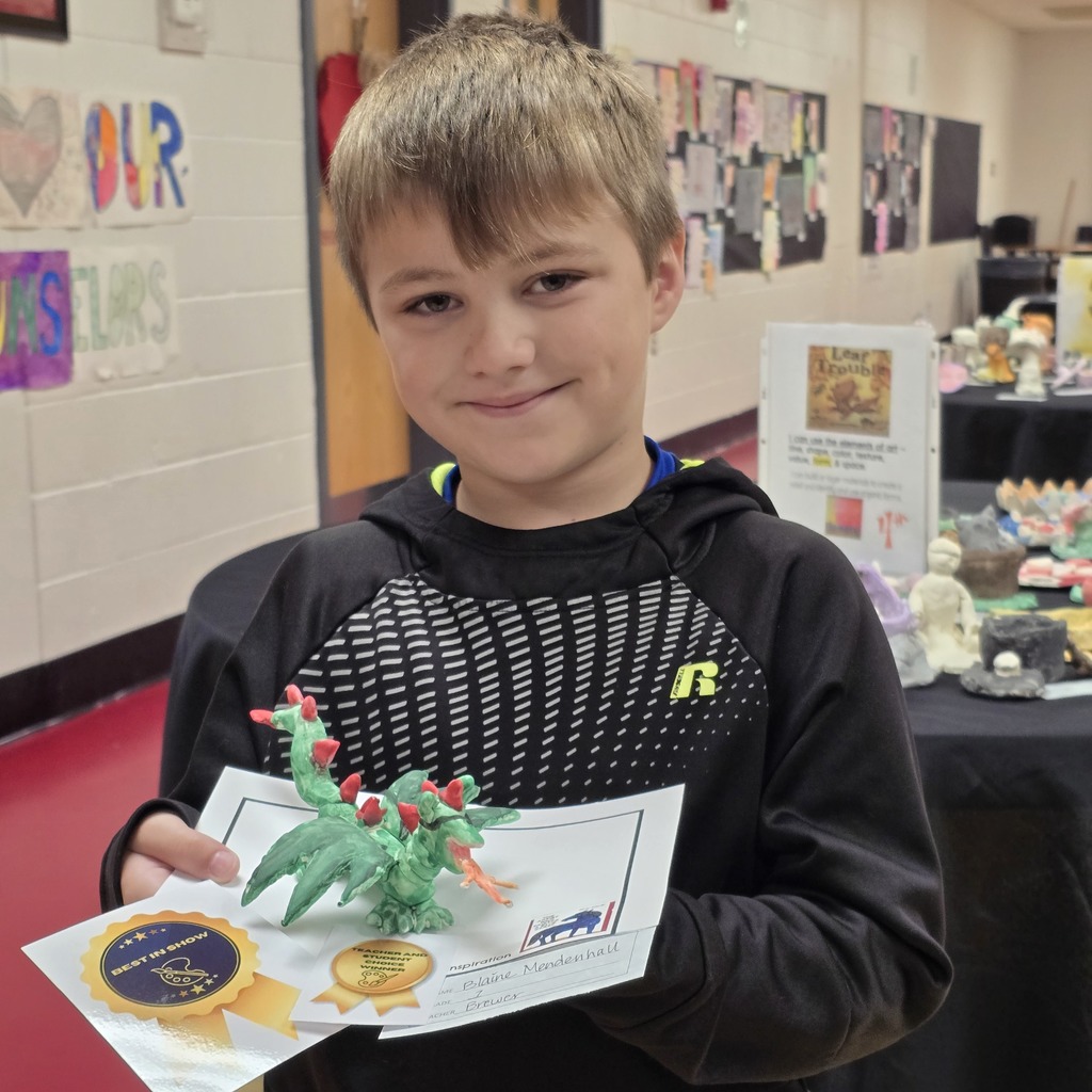 Boy holds a green dragon award. A black table with a display is in the background.