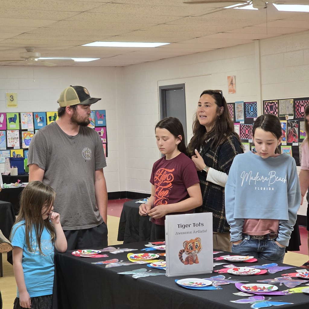 A group of people standing around a table covered in plates and artwork. A sign is displayed.