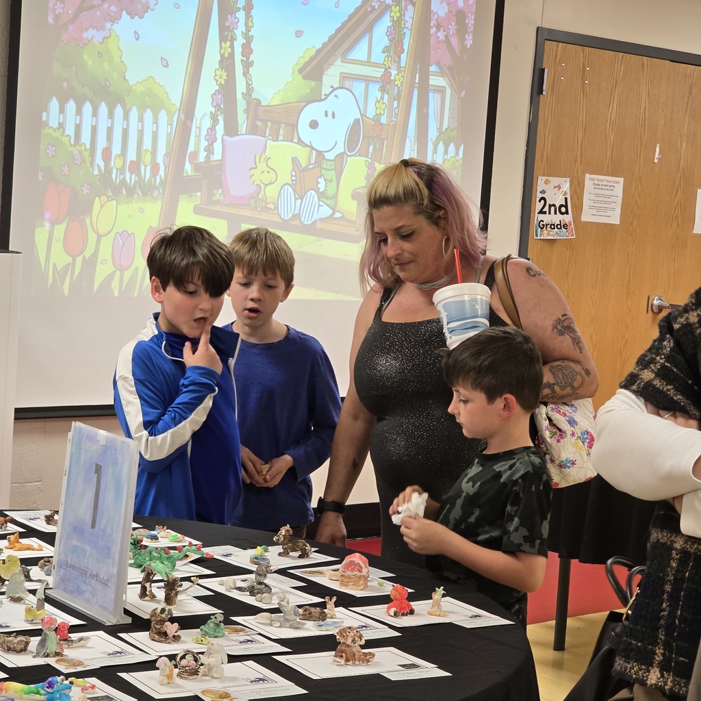 Display of cupcakes at a table, with a group of kids and a woman, under a projector screen.