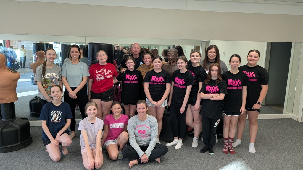 A group of people, wearing similar T-shirts, poses for a photo in a gym or studio.