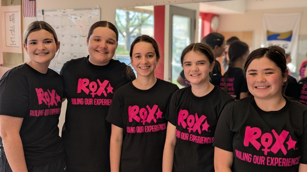 Five girls wearing black t-shirts with pink lettering that reads "ROX." They stand next to each other.