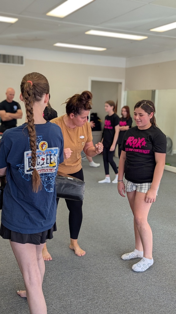 Several people in a room with a mirror, two wearing blue shirts, one in a brown shirt, and one wearing white shoes.