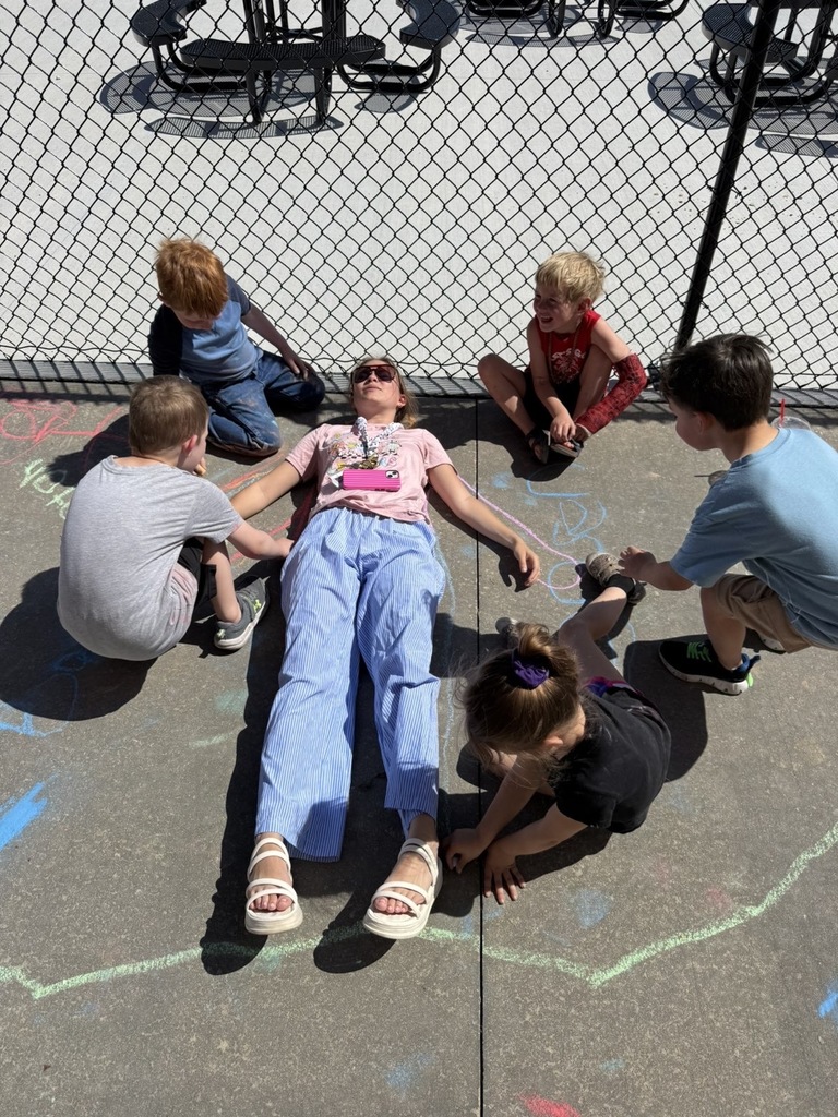 A woman lies on her back on the ground with four children around her, all in a shaded area.