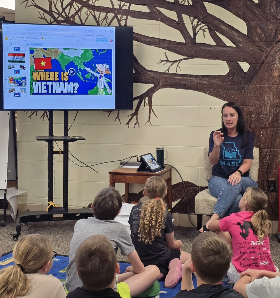 Group of students sit around a teacher in a classroom; screen shows map with 'Where is Vietnam?'