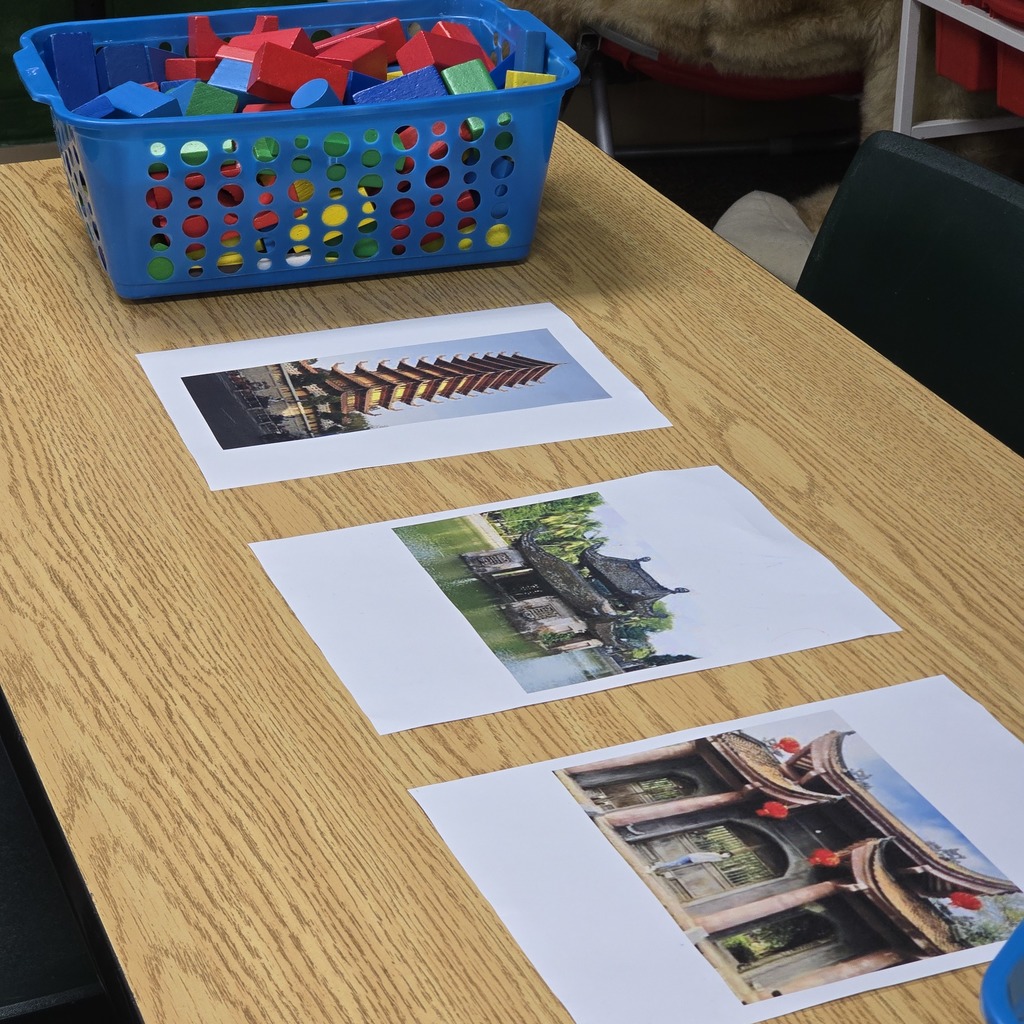 A wooden table with three cards, each displaying a picture of a different architectural structure. A blue basket filled with colorful building blocks sits on the table.