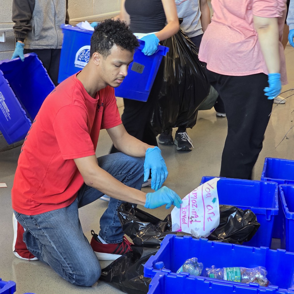 A man in a red shirt kneels sorting items into plastic bins with others around him.