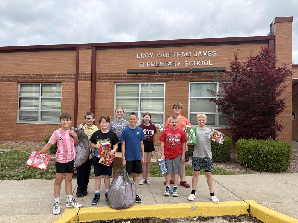 A group of children holding bags and boxes standing in front of Lucy Vaughan James Elementary School.