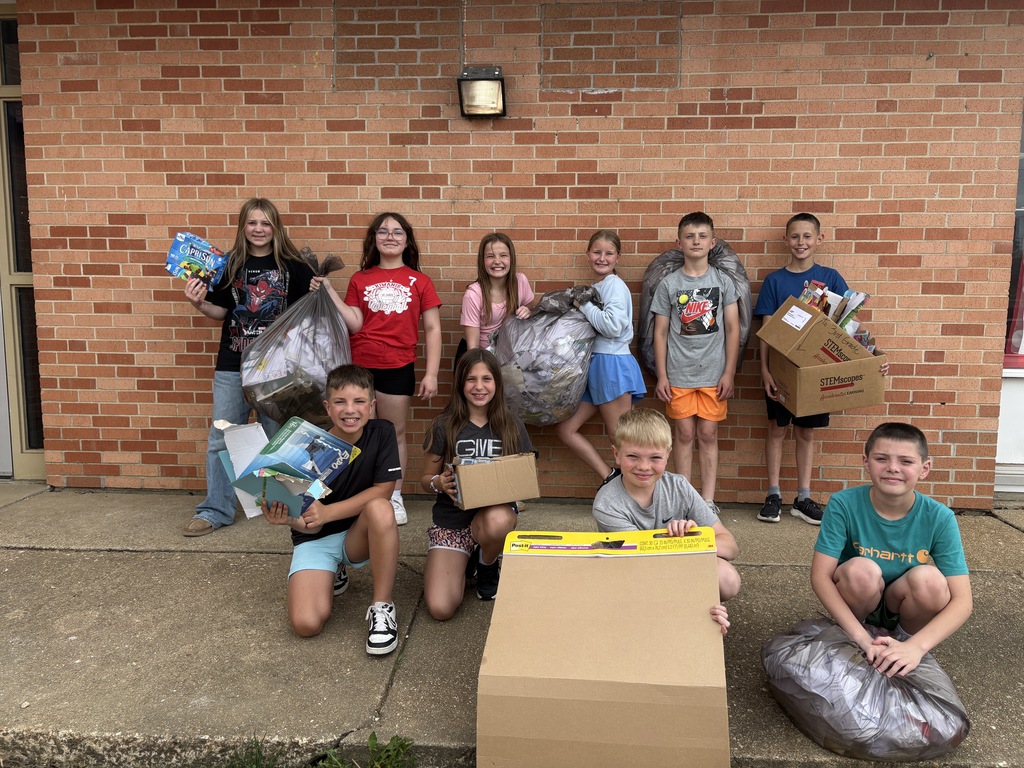 A group of children pose outside a brick building, holding boxes and bags, possibly for a charity event.