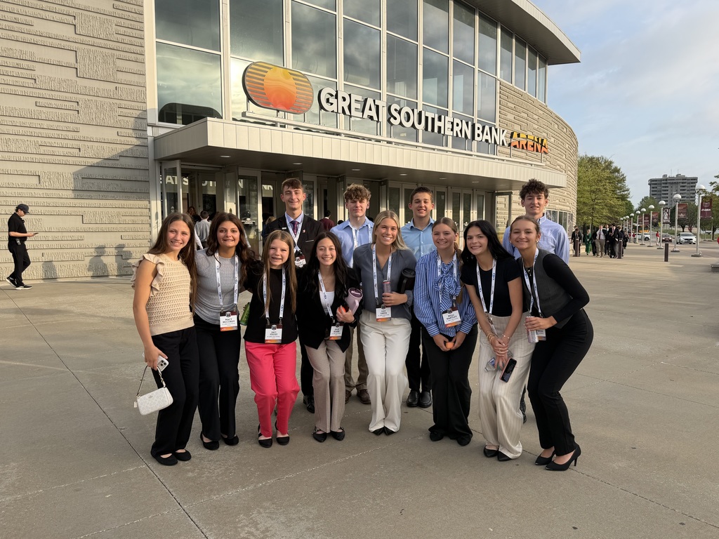 A group of people in formal clothing stand outside the entrance to a building with a logo.