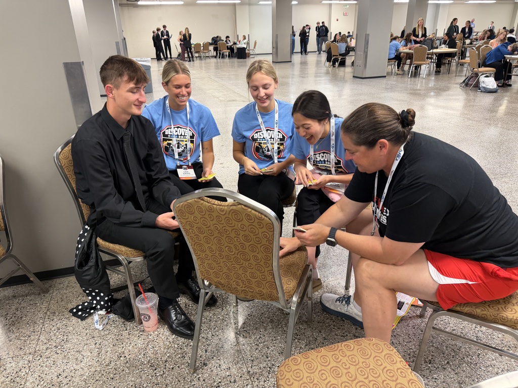 Five people sit around a chair in a conference room. A woman looks at a man's fingers.
