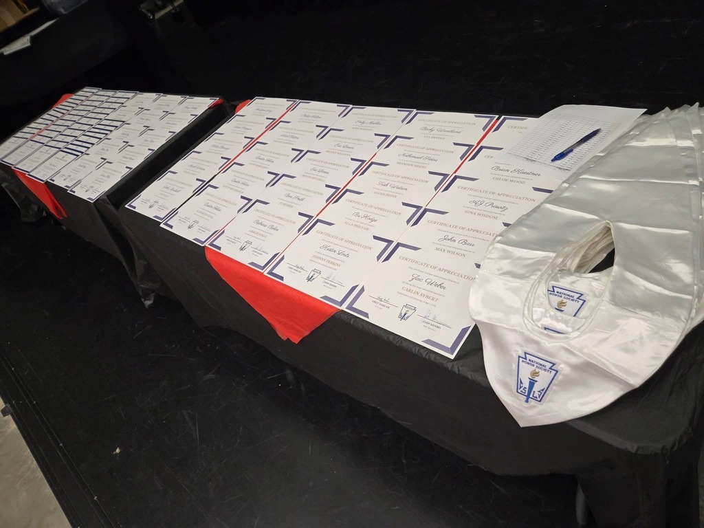 A table with folded documents and white garments on black cloth. A red cloth covers the table's center.