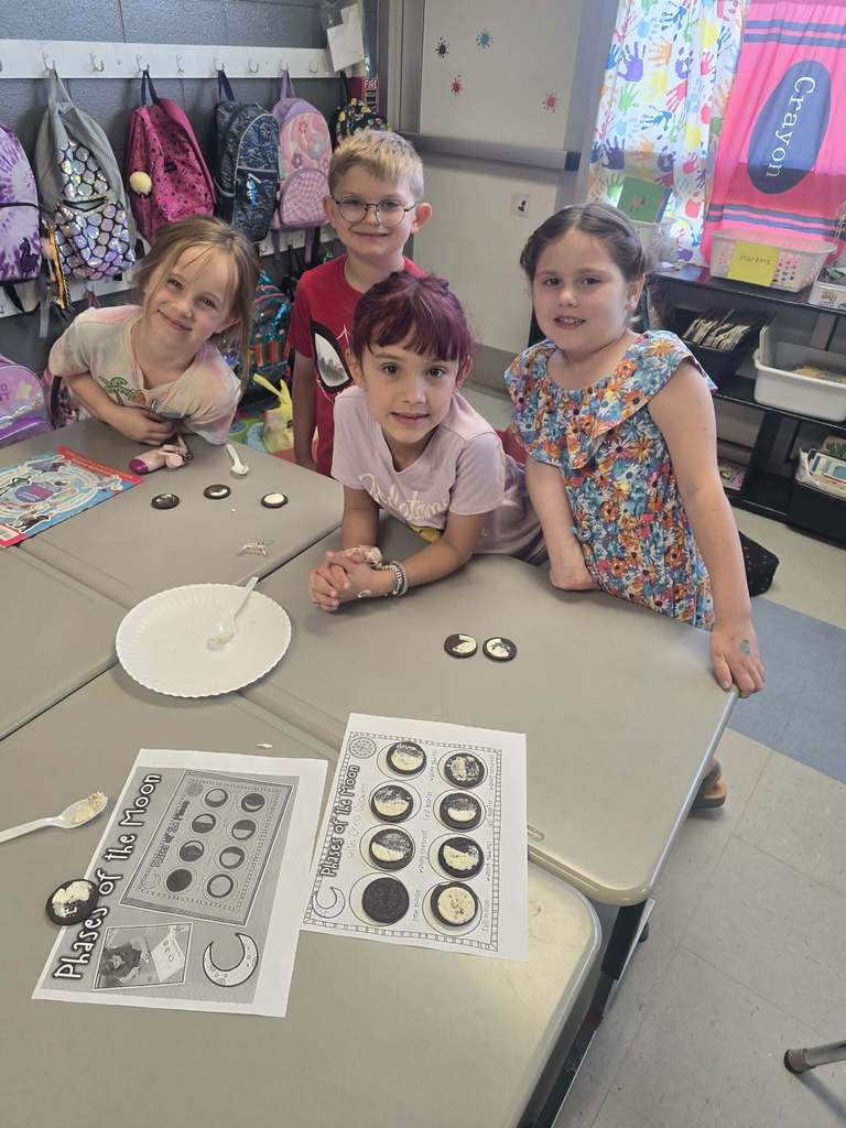 Four children at a table with a plate and papers showing moon phases.