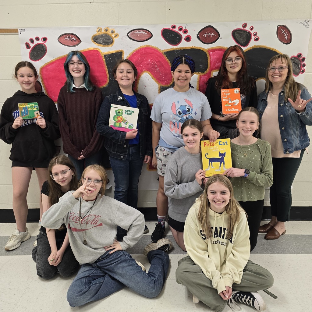 A group of young people pose for a photo, holding books, in front of a wall with paw prints.