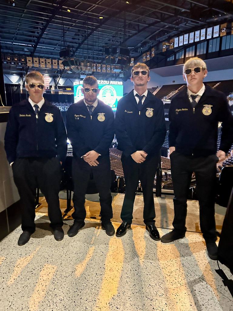 Four men in uniform stand in an arena with bright overhead lights, facing the camera.