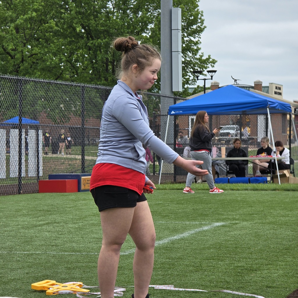 A woman in a blue top and red shorts prepares to throw a yellow object on a sports field.