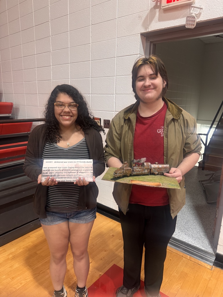 Two people stand in a gym, smiling, with one holding a certificate and the other holding a model.