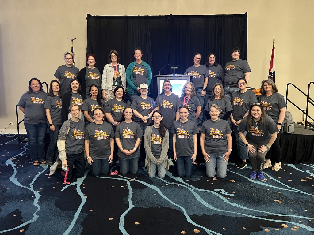 A group of people in matching shirts posing for a photo in a room with a stage.