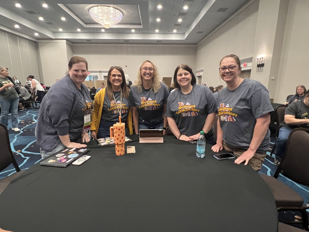 Five people in matching gray shirts pose around a round table with a game and a bottle.