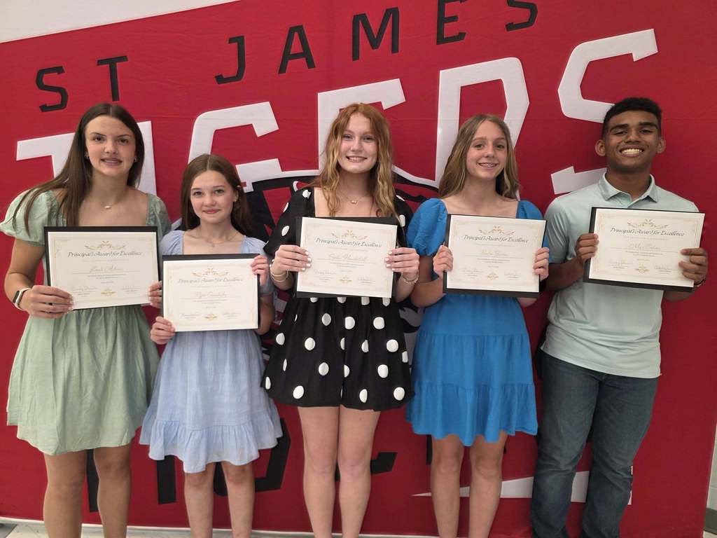 Five individuals stand together with framed certificates; three women in dresses, one boy in a polo shirt, and a red sign reading "St. James" in the background.