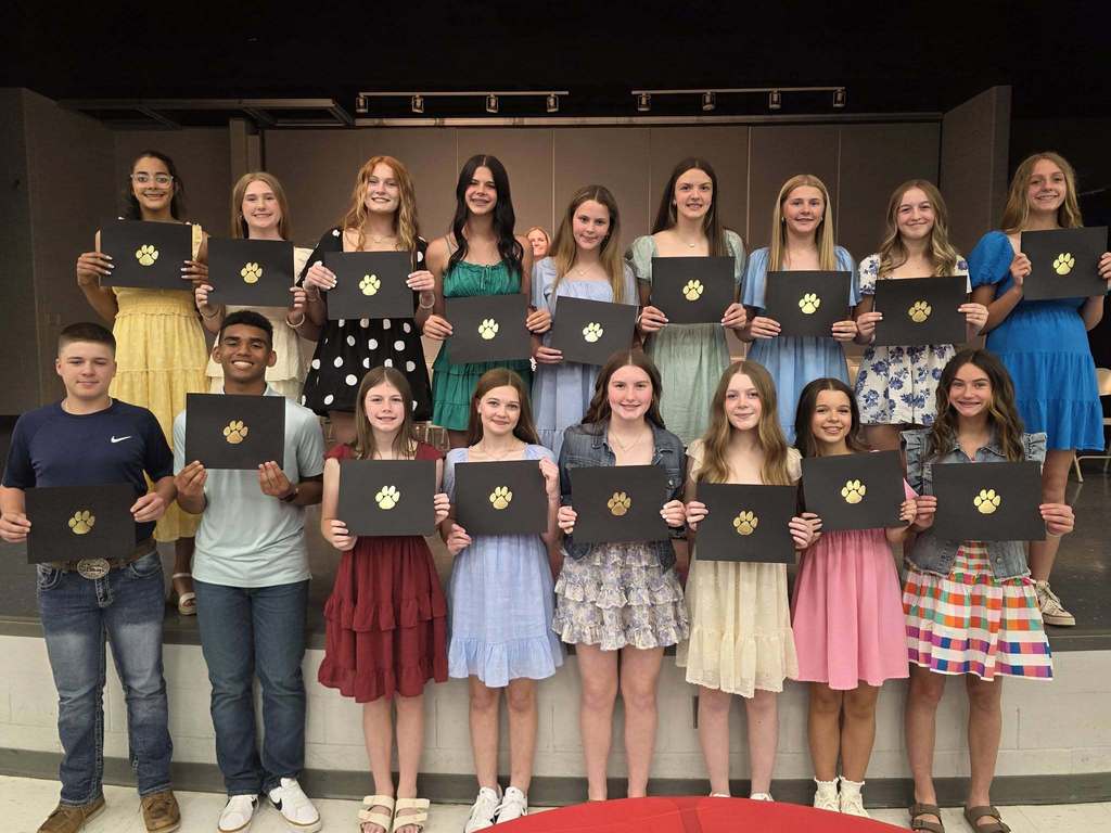 A group of students holding certificates stands on a stage, smiling and looking at the camera.