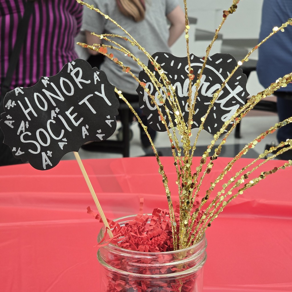 A red table with a jar of shredded paper and a centerpiece of gold sticks and a sign reading "Honor Society".