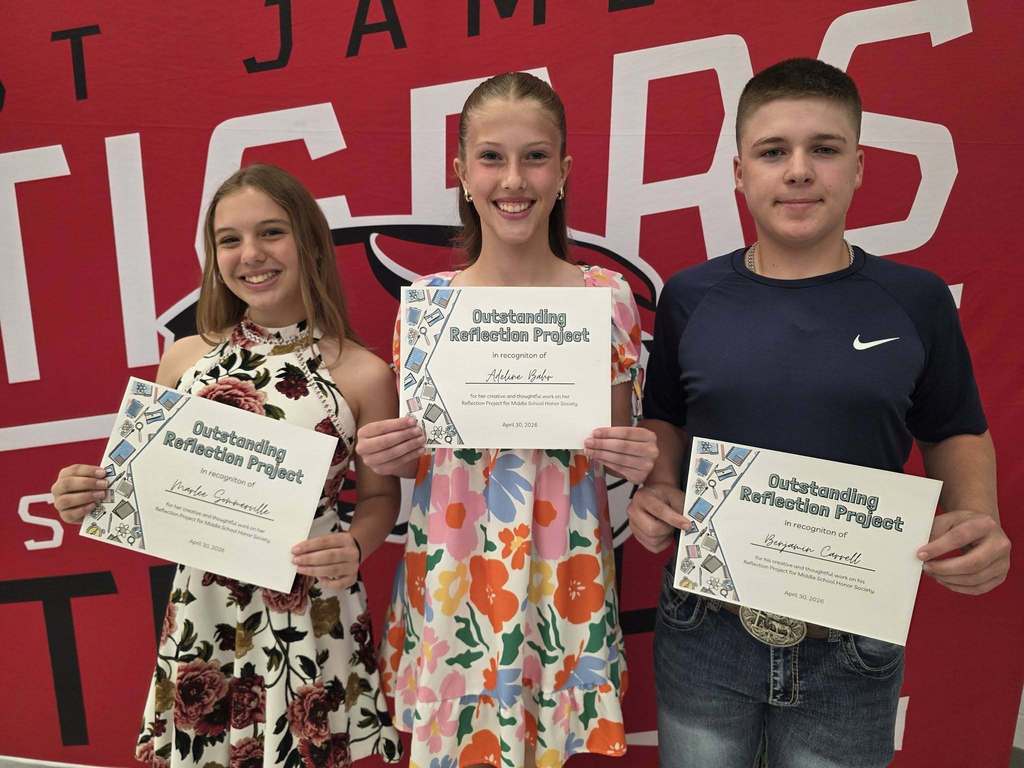 Three individuals stand holding certificates, with one in the middle wearing a floral dress. Behind them is a red backdrop with "JAMAS" and "TICS" text.