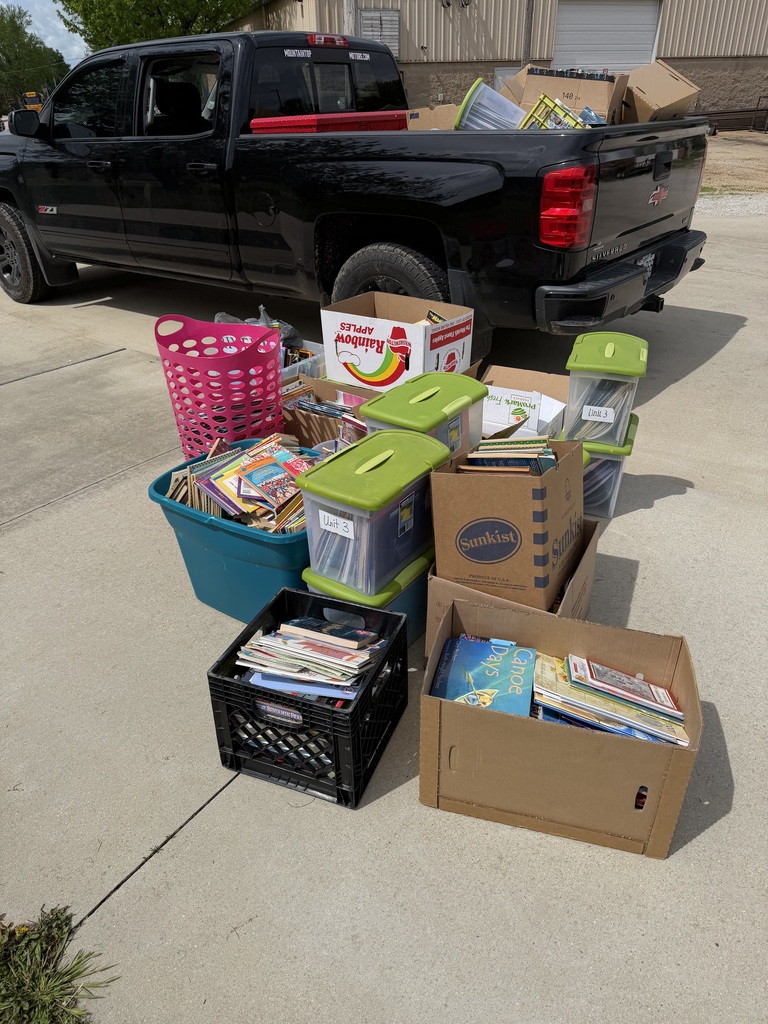 A black pickup truck parked on a driveway with several storage boxes and bins full of books.