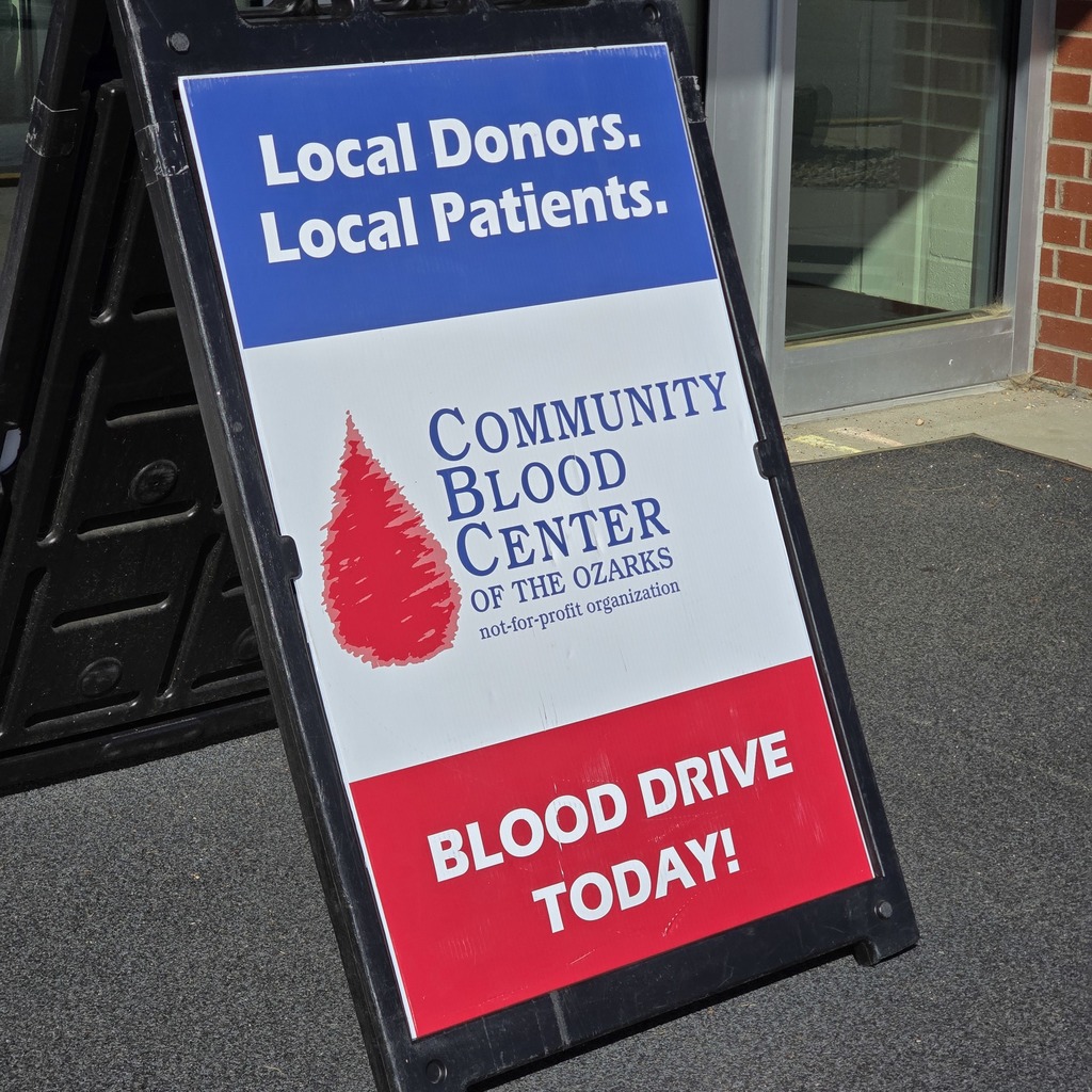 Sign with "Local Donors. Local Patients." and "Blood Drive Today!" on a sidewalk in front of a building.