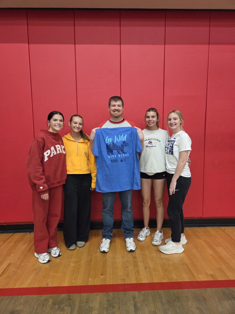 Five people stand on a wooden floor in a room with red walls, posing with one person holding a blue shirt.