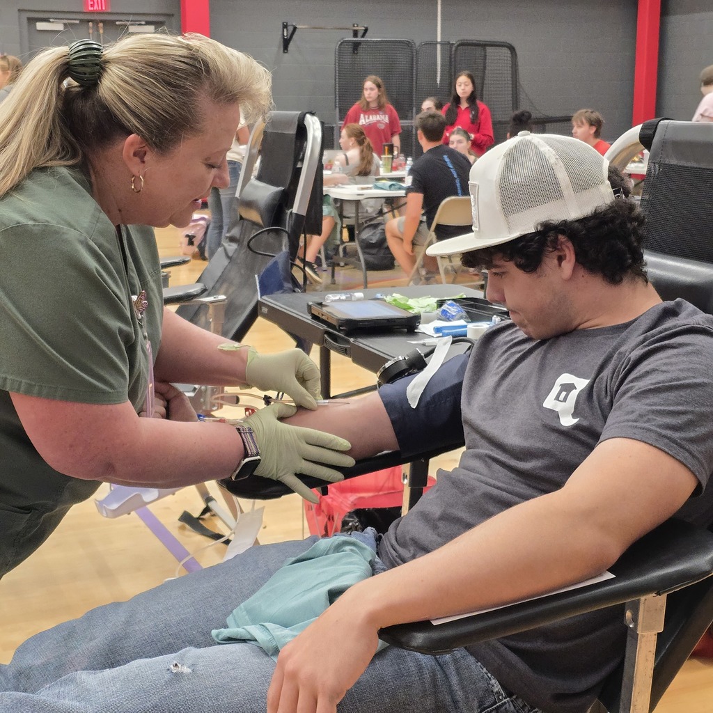 A seated person has a blood pressure cuff on their arm. A woman checks the cuff.
