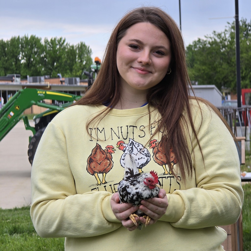 Woman in a yellow shirt with printed chickens, holding a small chicken in her hands.