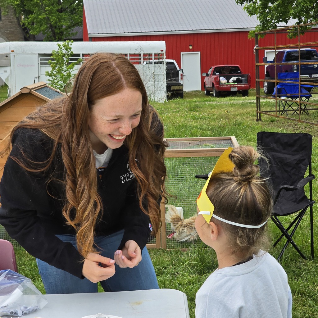 Woman with long hair smiles and shows a child wearing a yellow visor an item.