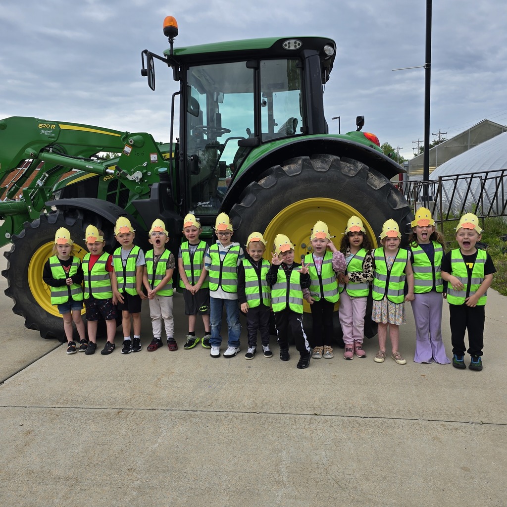 Group of children in yellow safety vests and hats posing in front of a large tractor.