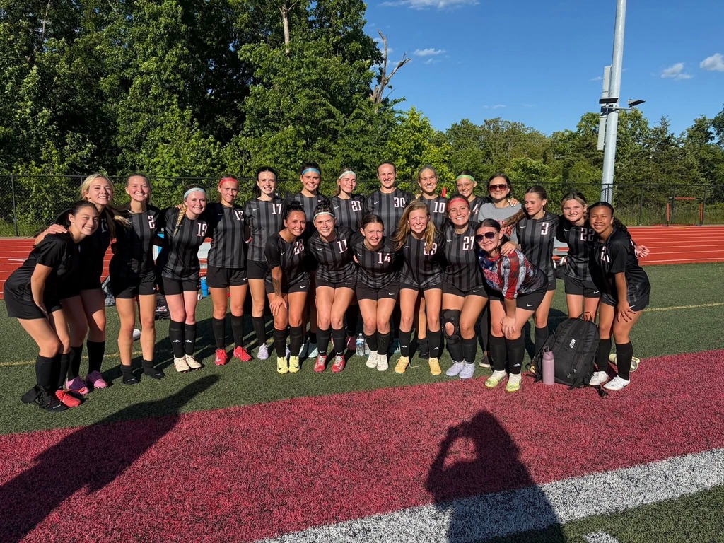 A soccer team in black uniforms poses for a group photo on a field with red and white markings.
