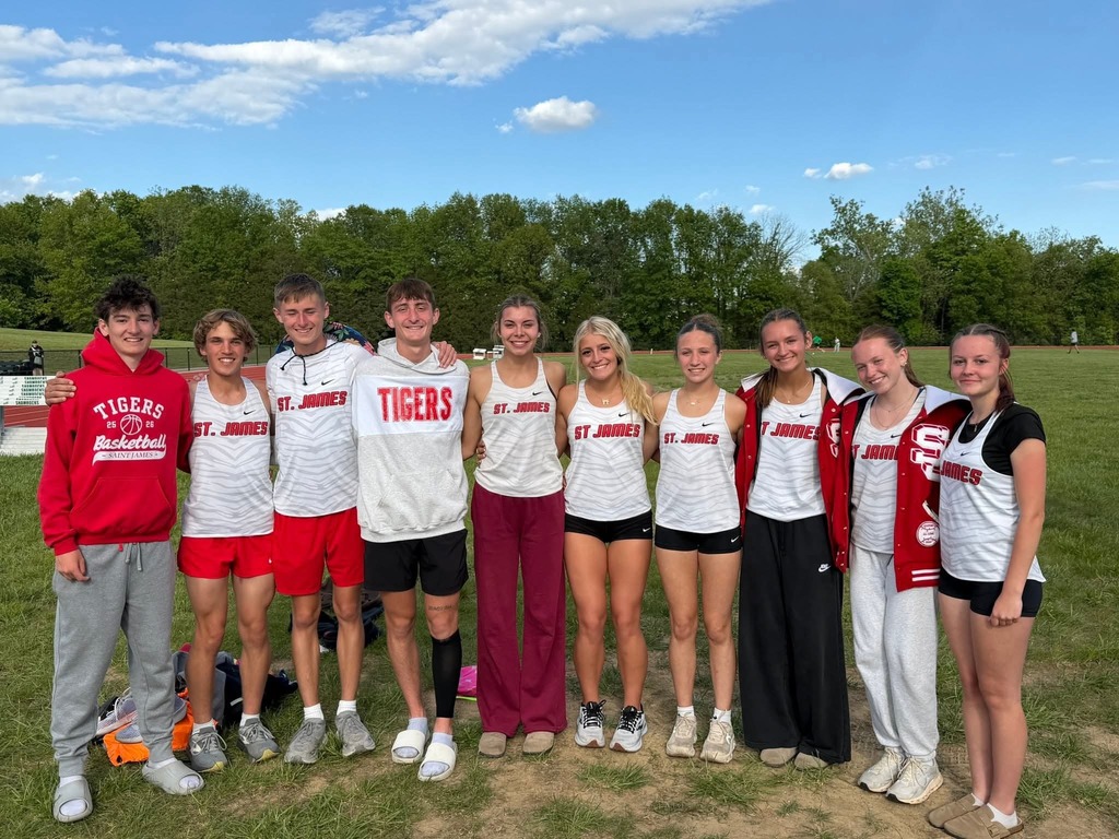 A group of athletes in matching white and red uniforms pose for a photo on a grassy field.