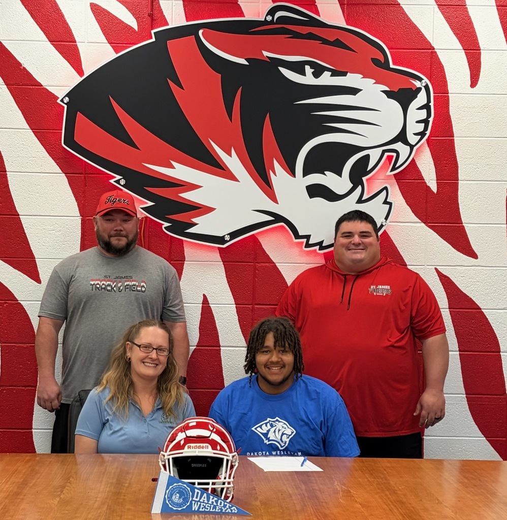 Four individuals pose behind a table with a helmet; two in red, one in blue, and one in gray. A tiger logo is in the background.