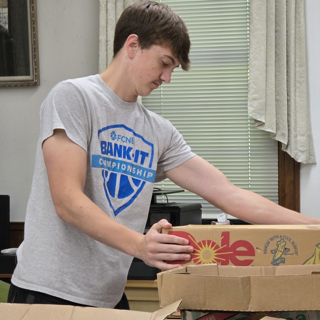 A person wearing a gray shirt with the text "BANK IT CHAMPIONSHIP" handles boxes.