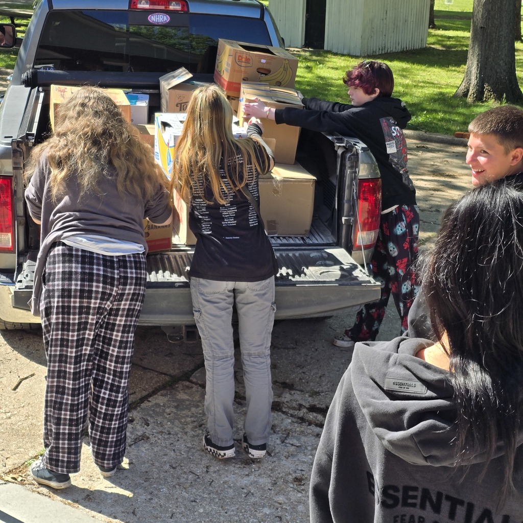 Several people unload boxes from a pickup truck. One person wears a hoodie and pants, another wears pajamas.