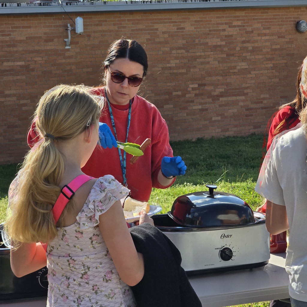 People gathered around a table with a slow cooker, one wearing blue gloves and a red shirt.