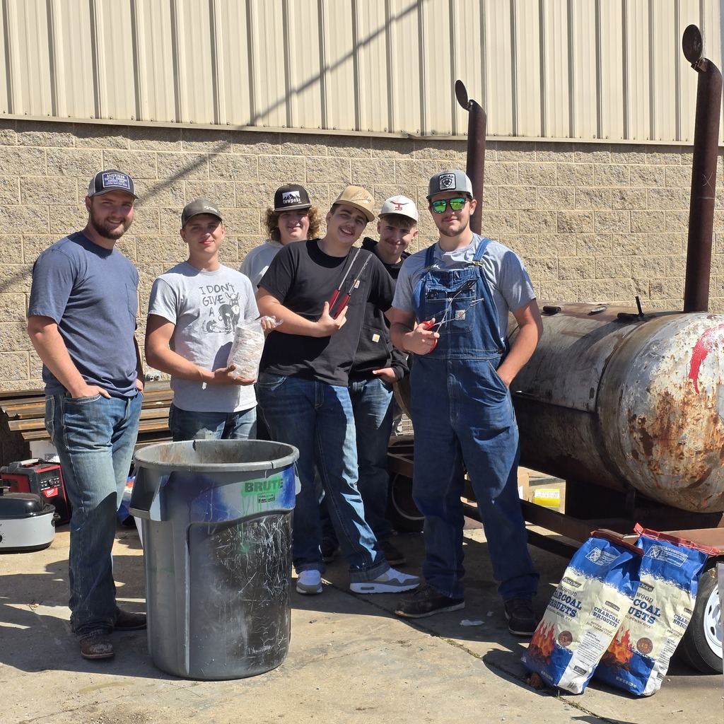 Five men in casual attire stand outside, next to a barrel and a rusty tank, holding various items.