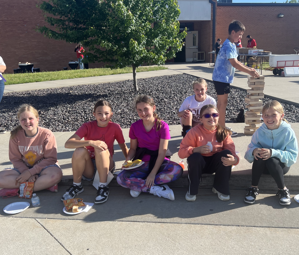 Six girls sit on a sidewalk with food.